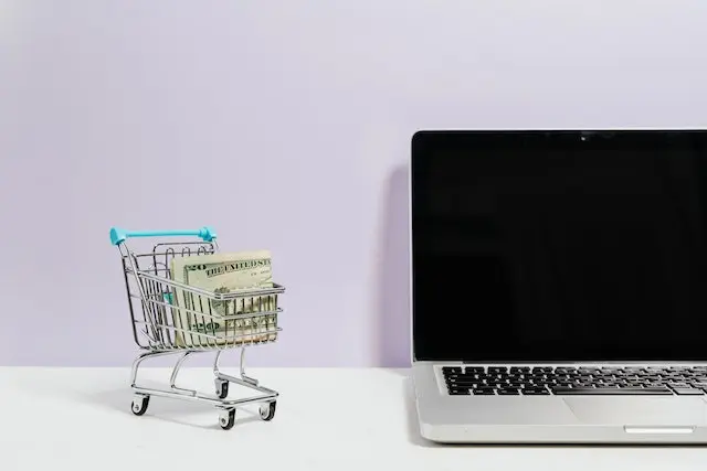 A laptop and a cart of money next to it